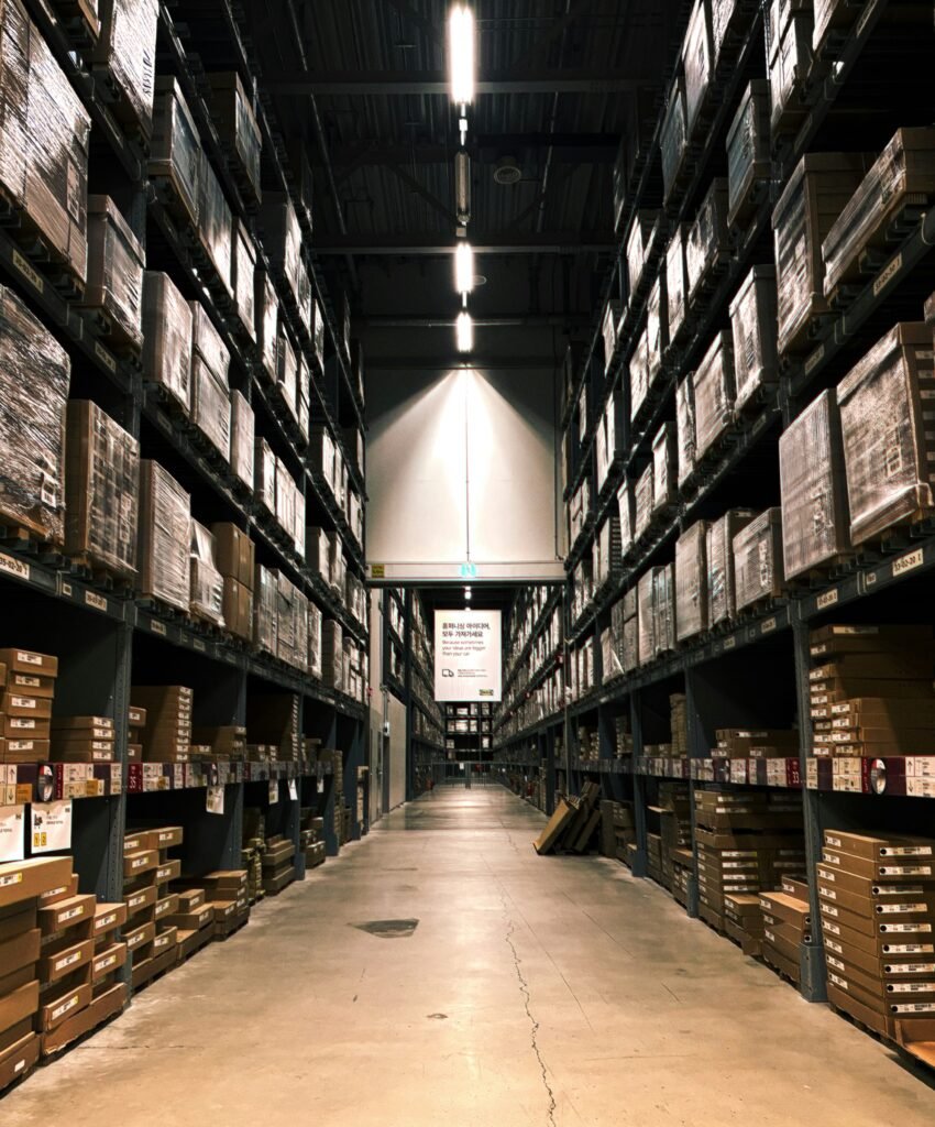 Warehouse interior with tall shelves stacked with boxes and pallets, illustrating the importance of compliance in warehouse permit applications.